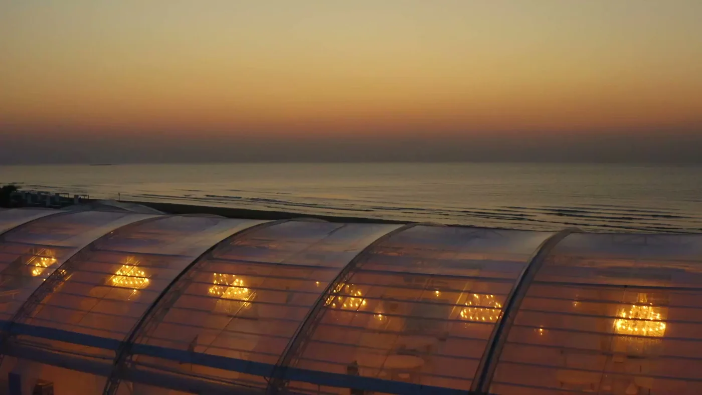 שקיעה מעל הים הכספי וגג הזכוכית הזוהר של ביתן חוף