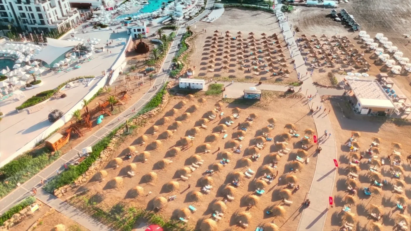 Qürub işığında Sea Breeze çimərliyi: saman çətir sıraları və dənizə cığırlar, yüksəklikdən görünüş